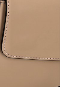 Borsa a mano in pelle beige con texture liscia, caratterizzata da bordi neri a contrasto e cuciture bianche dettagliate lungo le giunture.