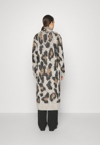 Dlhý pletený kardigán v krémovej, čiernej a hnedej farbe s leopardím vzorom. Mäkká textúra s rebrovaným vzorom, otvorený dizajn a dlhé rukávy.