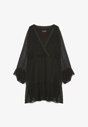 Blusa negra con escote en V, mangas largas abullonadas y un bajo con volantes en capas. Hecha de un tejido translúcido con una textura y un patrón de puntos.
