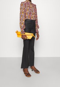 Blomstret bluse med flæset krave, sorte højtaljede bukser og en gul clutch. Sorte strop-sandaler med en lille hæl.