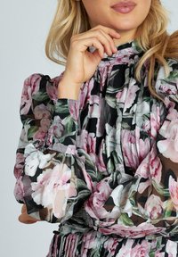 Transparante blouse met bloemenpatroon en ruches aan de mouwen in zwart, roze en groen. Kenmerkt zich door een hoge hals en gathered boorden voor extra textuur.