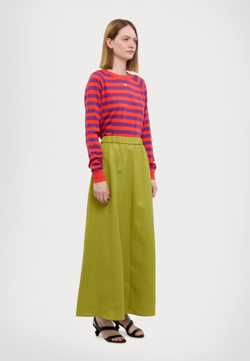 Camicetta a maniche lunghe a righe rosse e viola abbinata con una gonna maxi verde. L'outfit ha una vestibilità comoda ed è completato da sandali neri con cinturini.