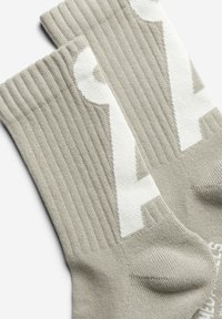 Graue gerippte Socken mit weißem Logo. Die weiche Strickstruktur und die kontrastierenden Akzente an den Bündchen und Seiten steigern das visuelle Interesse.