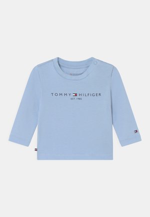 Vaaleansininen pitkähihaineen paita, joka on valmistettu puuvillasta. Ominaisuuksiin kuuluu pyöreä kaula-aukko, nappi olkapäällä ja "TOMMY HILFIGER EST. 1985" -teksti painettuna etupuolelle.