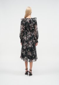 Čierne kvetinové šaty s dlhými rukávmi, volánikmi na ramenách a viaczónovou sukňou. Má priehľadnú textúru a jemné vzorované detaily.