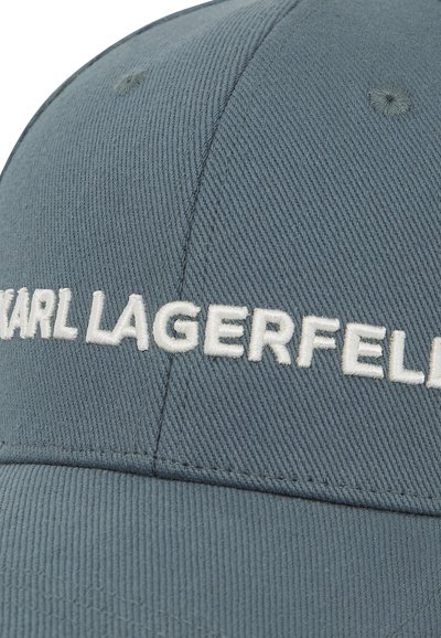 Casquette en toile grise avec le texte "KARL LAGERFELD" brodé en blanc. Présente un design structuré et des détails de coutures visibles.
