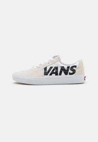 Beiga mocka skateboardskor med en vit mesh-tunga. Stort svart "VANS"-logga på sidan, vita snörningar och vit gummi-sula.