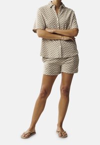 Beige short-sleeve shirt and matching shorts with a herringbone pattern. The fabric appears lightweight and textured, paired with tan flip-flops.