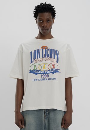 Biała bawełniana koszulka z kolorowym napisem graficznym "LOW LIGHTS CHAMPIONSHIP 1999" z niebieskimi, zielonymi i czerwonymi akcentami. Krótkie rękawy.