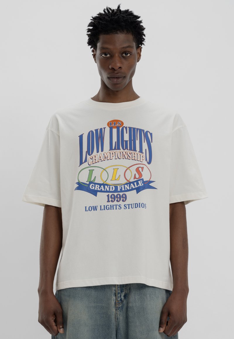 Weißes Baumwoll-T-Shirt mit buntem Grafiktext "LOW LIGHTS CHAMPIONSHIP 1999" in Blau-, Grün- und Rotakzenten. Kurze Ärmel.