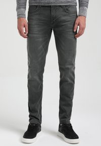 Jeans de mezclilla gris con un corte ajustado. Cuenta con cinco bolsillos, un ligero desgaste y costuras visibles. Combinados con zapatillas negras.