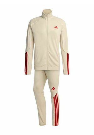 Tuta sportiva beige con strisce rosse sulle maniche e sulle gambe, giacca con zip completa e logo Adidas su petto e coscia.
