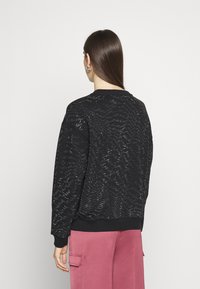 Sudadera negra con un patrón de olas texturizado, puños y dobladillo acanalados. Combinada con pantalones cargo rosas, mostrando un diseño simple y casual.