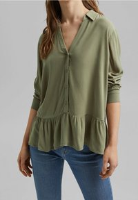 Blusa verde oliva con bottoni, colletto, maniche lunghe e orlo arricciato. Realizzata in tessuto leggero con una texture liscia.