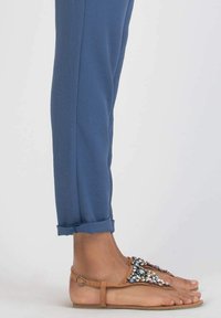 Tan sandals with decorative gems, flat sole, and ankle strap. Light blue, cuffed pants with a soft texture and slim fit.