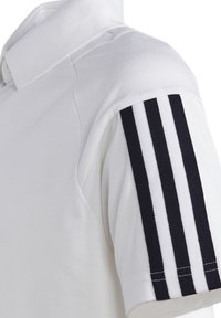 Weißes Polohemd mit strukturiertem Oberflächenmaterial, das an der Schulter einen schwarzen Streifenakzent aufweist und einen klassischen Kragen hat.