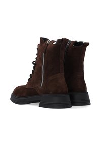 Hnědé semišové kotníkové boty s šněrováním na přední straně a bočními zipy, s výraznou černou gumovou podrážkou a zesíleným prošíváním.