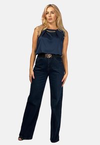 Granatowy satynowy top bez rękawów z detalami w postaci łańcucha, zestawiony z ciemnymi dżinsami o wysokim stanie w szerokim kroju, akcentowany czarnym paskiem z metalową klamrą.