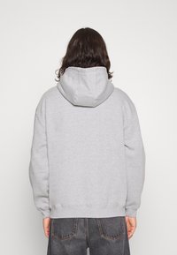 Hoodie in lichtgrijs, met een zachte textuur, elastische boorden en een relaxte pasvorm. Het ontwerp bevat een eenvoudige achterkant en minimale details.