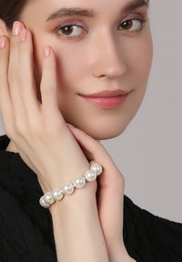 Pearl bracelet featuring round, glossy white beads, securely strung, worn on a slender wrist, complemented by a textured black top.
