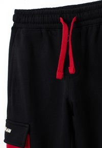 Pantalones de chándal negros con cordones rojos, con bolsillos laterales y un puño doblado. El material es suave con un ligero brillo, logotipo en el puño.