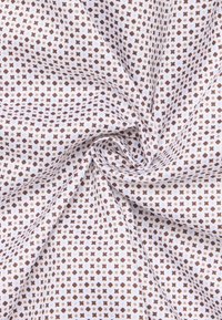 Tessuto di cotone con uno sfondo bianco che presenta un motivo ripetitivo di piccoli punti marroni e forme a croce, con una finitura liscia.