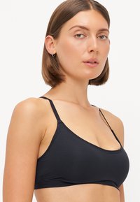 Černý bralet vyrobený z měkké tkaniny s tenkými nastavitelými ramínky, trojúhelníkovými košíčky a čistým švem. Minimalistický design bez ozdob.