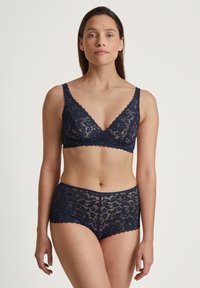 Marinblå spetsunderkläder med en v-ringad bralette med vågiga kanter och matchande högmidjade trosor med blommönster.