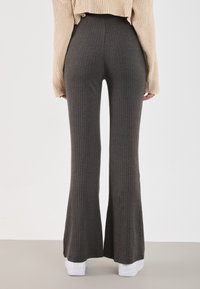 Pantalons évasés en velours côtelé charbon, fabriqués en tissu doux, avec une taille haute et une finition texturée. Assortis à des baskets blanches.