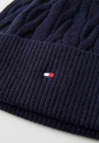 Marine gebreide beanie met kabelpatroon, geribde boord en een klein geborduurd logo met rode, witte en blauwe strepen.