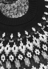Sorte og hvide strikkede sweater med rund halsudskæring, prydet med geometriske mønstre, herunder diamanter og zigzag-mønstre på brystet.