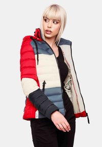Doudoune avec des panneaux rouges, bleu marine et crème, accents noirs et fermeture éclair. Comprend une capuche et un détail graphique intérieur.