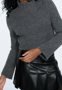 Grau geripptes Strick-Turtleneck-Oberteil mit langen Ärmeln, taillierter Schnitt, getragen über einem schwarzen plissierten Rock aus Kunstleder mit glatter Oberfläche.