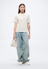 Κρεμ κοντομάνικη μπλούζα με το λογότυπο "BOSS", συνδυασμένη με ανοιχτό μπλε τζιν παντελόνι φαρδιάς γραμμής και μικρή μπεζ τσάντα χειρός. Λευκά αθλητικά παπούτσια ολοκληρώνουν την εμφάνιση.