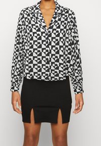 Chemise boutonnée noir et blanc avec un motif de cœur géométrique et des manches longues. Associée à une jupe noire ajustée avec des fentes sur les côtés.