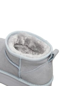 Botină din suede gri, cu căptușeală moale din blană gri, accente albastre deschise și o mică buclă la spate pentru o încălțare ușoară. Prezintă cusături întărite.