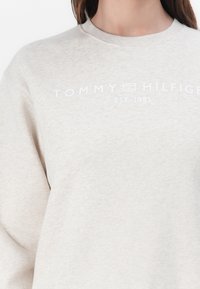 Lichtbeige sweatshirt van zachte stof. Voorzien van een ronde hals, ribgebreide manchetten en een bedrukt logo "TOMMY HILFIGER EST. 1985" in het wit.