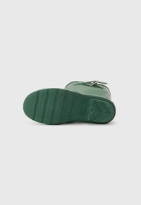 Grønn gummistøvel med teksturert såle. Har en blank finish, rund form og metallbeslag for lukking. Merkevaren er preget på sålen.