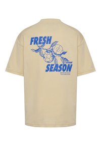 Beżowy bawełniany T-shirt z niebieskim graficznym wzorem z napisem „FRESH SEASON”, motywami sportowymi i liściastymi akcentami na plecach.
