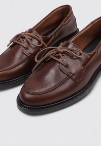 Zapatos de cuero marrón con punta redondeada, diseño de cordones y detalles sutiles de costura. Suela de goma negra que proporciona tracción y durabilidad.