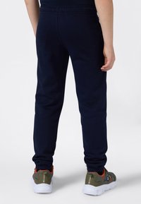 Marineblauwe trainingsbroek met een elastische tailleband, taps toelopende pijpen en geribbelde boorden, gecombineerd met grijze en oranje sportschoenen.