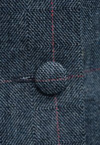 Tkanina w pepitkę w odcieniach niebieskiego i szarości, z okrągłym guzikiem i kontrastującymi czerwonymi przeszyciami wzdłuż szwów.