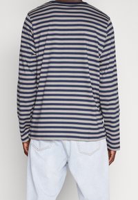 Camiseta de manga larga a rayas en azul marino y beige, con cuello redondo, corte recto y tela suave. Combinada con jeans de color azul claro.
