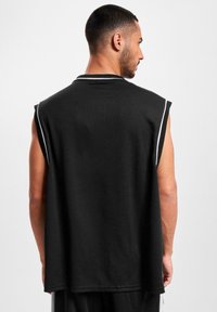 T-shirt sans manches noir avec une coupe ample, fabriqué en tissu texturé. Présente une bordure blanche le long du col et des emmanchures. Vue arrière unie.