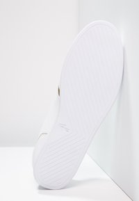 Bílá podrážka gumové tenisky s texturovanými protiskluzovými vzory a hladkým povrchem. Obsahuje jemný zlatý akcent a detail loga.