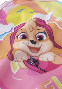 Cane in stile cartone animato con pelliccia bionda, occhiali rosa e un vestito rosa. Presenta un distintivo e uno sfondo colorato con nuvole e sole.