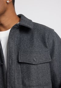 Gray wool shirt jacket featuring a pointed collar, a chest pocket with a black button, and a soft texture.