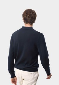 Navyblauer Strickpullover mit Kragen und gerippten Bündchen. Hat eine glatte Textur und eine taillierte Passform. Die Rückansicht zeigt Haare und einen schlichten Hintergrund.