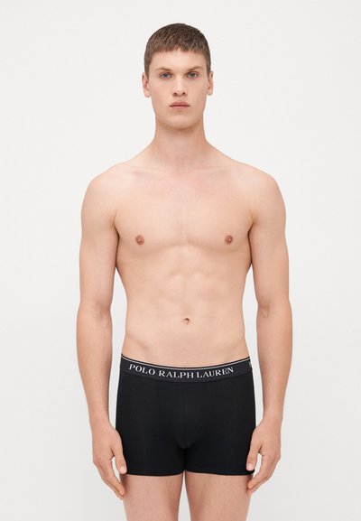 Boxer shorts pretos feitos de algodão com uma textura suave, apresentando uma faixa de logótipo branca contrastante na cintura. Modelo exibido sem camisa.
