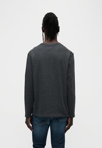 Μακρυμάνικο πουκάμισο σκούρου γκρι με στρογγυλή λαιμόκοψη, απαλής υφής και άνετη γραμμή, συνδυασμένο με μπλε τζιν.